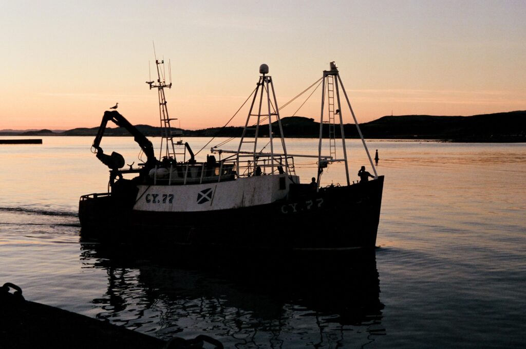Fishing boat on calm waters at sunset with silhouettes of distant hills in the background.