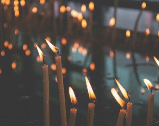 A dimly lit room filled with many glowing candles, casting soft light and shadows around the space.