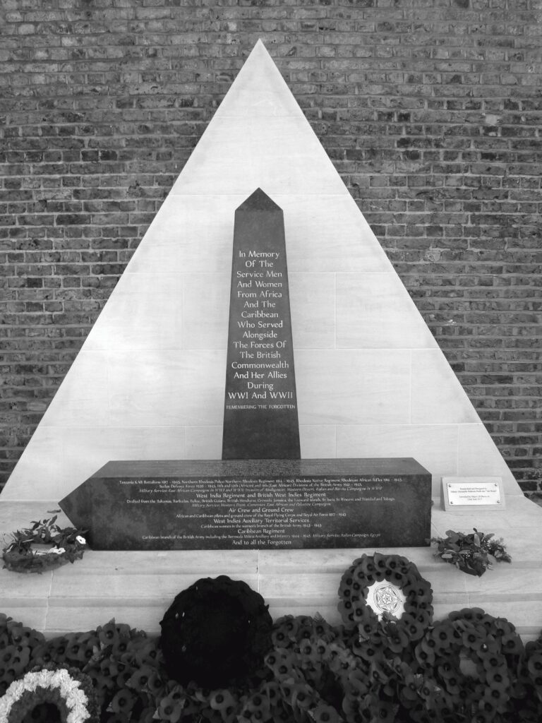 Black and white photo of the African and Caribbean War Memorial in Windrush Square, Brixton, adorned with a wreath.