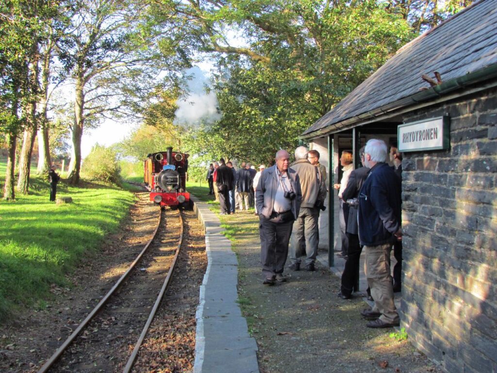 People gather by the train track while the Dolgoch locomotive, marked Rolt Explorer, nears Rhydyronen Station in Wales.
