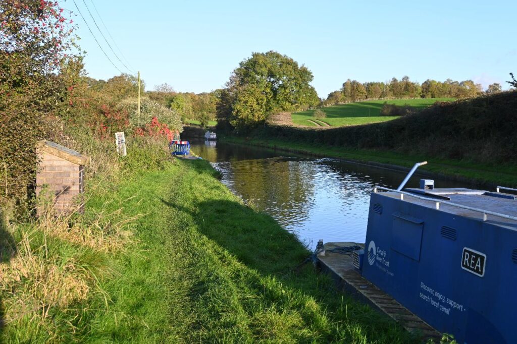 A blue boat moored on the Worcester & Birmingham Canal near Tardebigge, with grassy areas and a maintenance depot in the background.