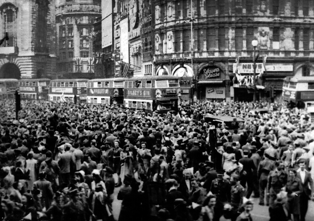A lively crowd fills Piccadilly, London, during VE Day celebrations, showcasing a festive spirit in the city street.