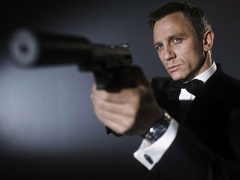 James Bond, portrayed by Daniel Craig, stands in a tuxedo with a gun, embodying sophistication and danger.