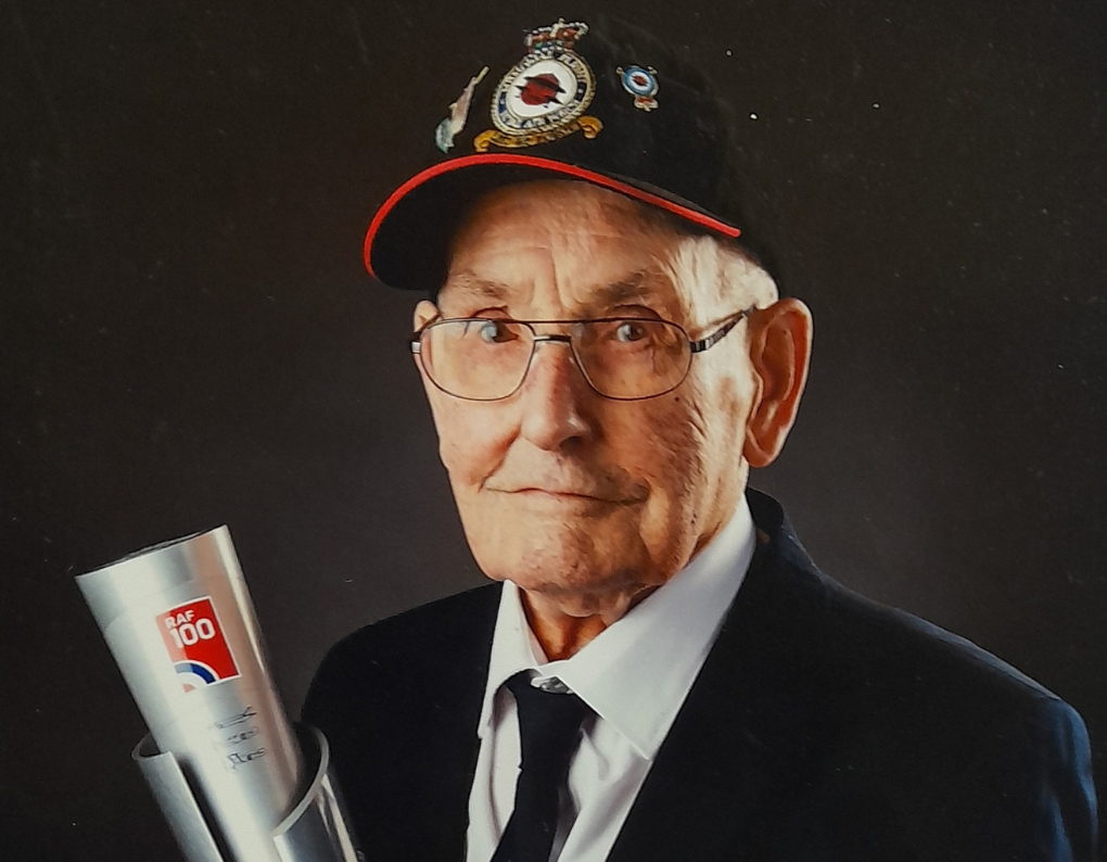 Fred Hooker, an older man in a suit, wears his war medals and displays an RAF 100 trophy with a proud expression.